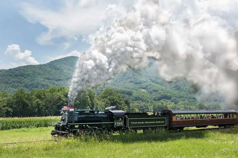 Great Smoky Mountains Railroad steam locomotive #1702 traveling through scenic mountain landscape with passengers aboard