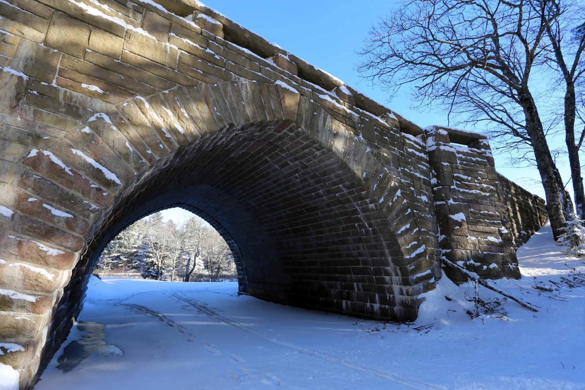 Snow-covered stone bridge on Acadia carriage road perfect for snowshoeing