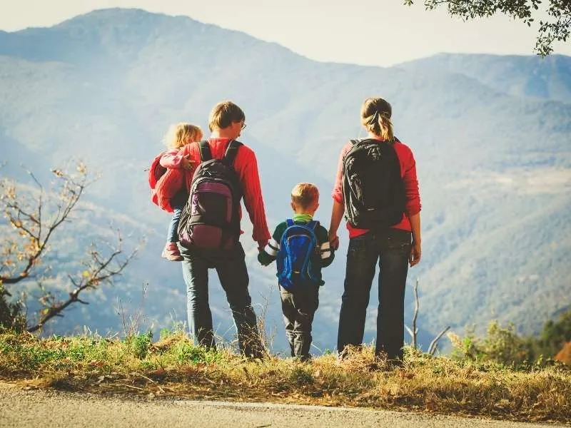 Happy family hiking together on a mountain trail with toddler and child
