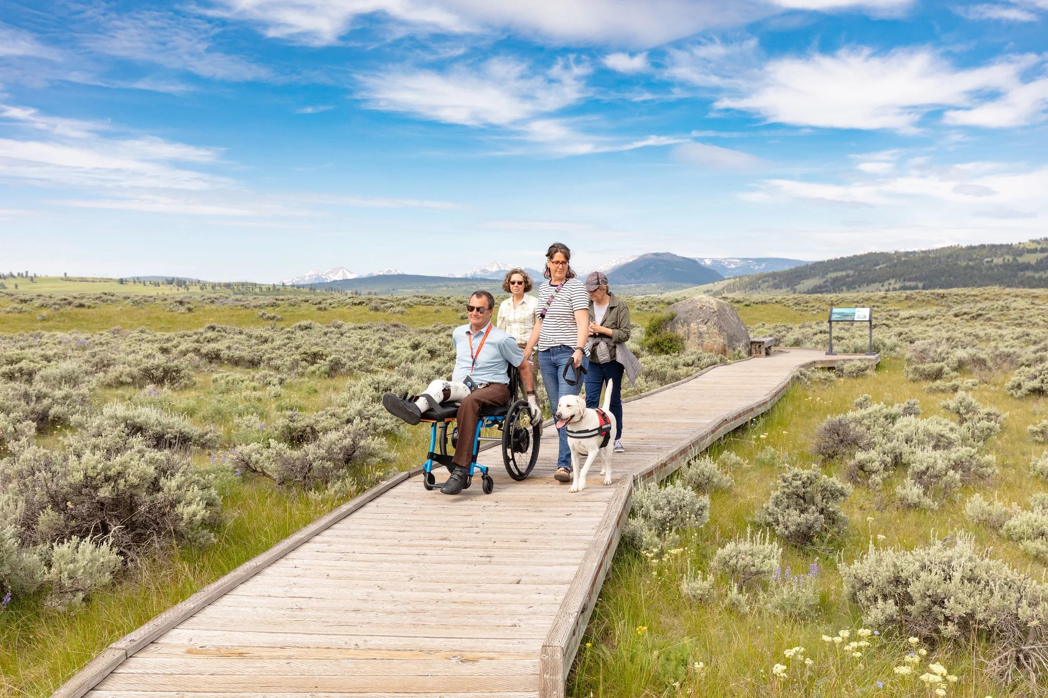 Accessible boardwalk trail at Yellowstone National Park with hikers using mobility aids enjoying the scenic mountain views