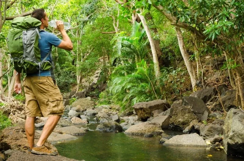 Hiker drinking water near a mountain creek during a hiking break