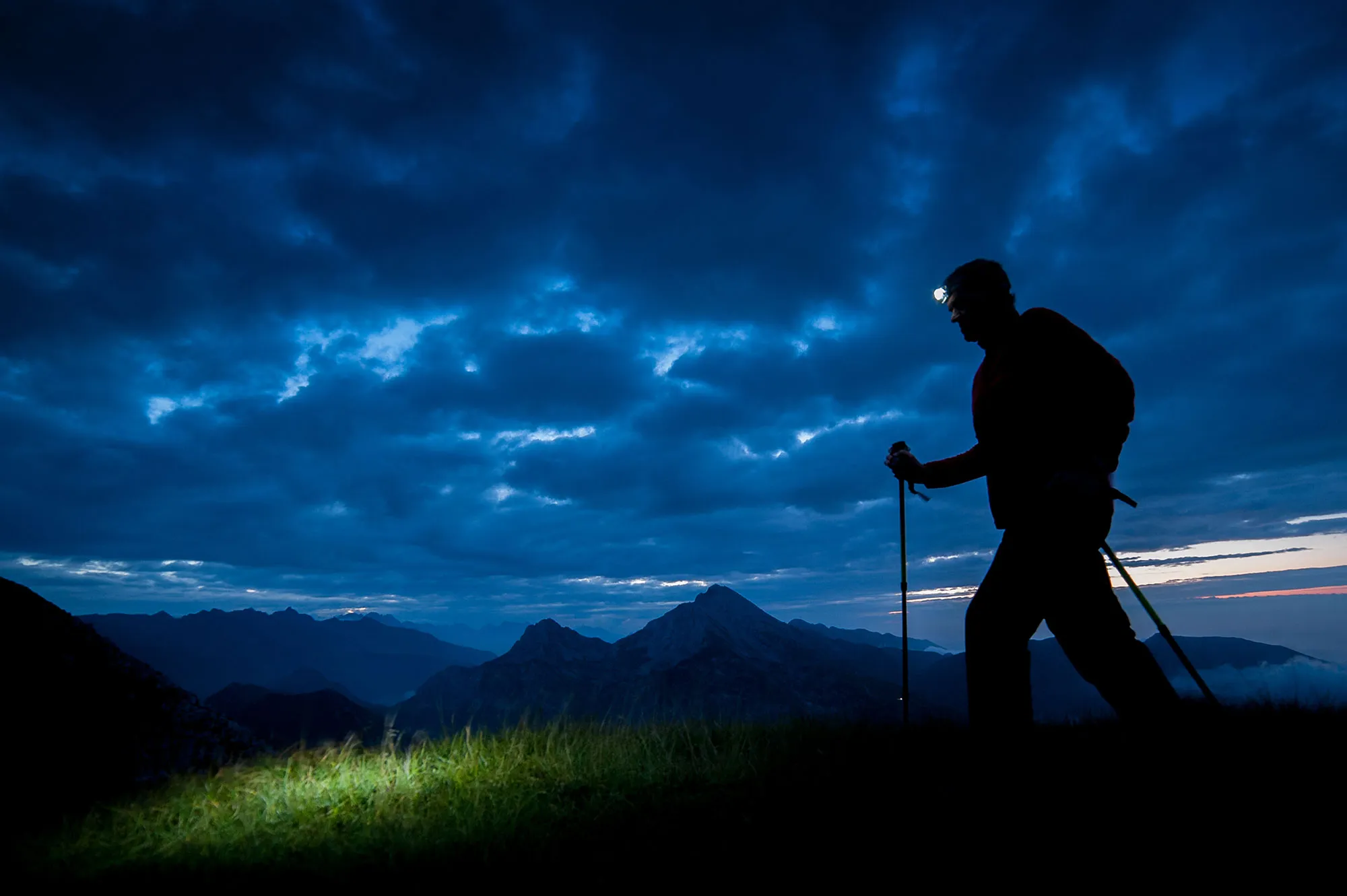 Night hiker using headlamp on mountain trail with safety gear