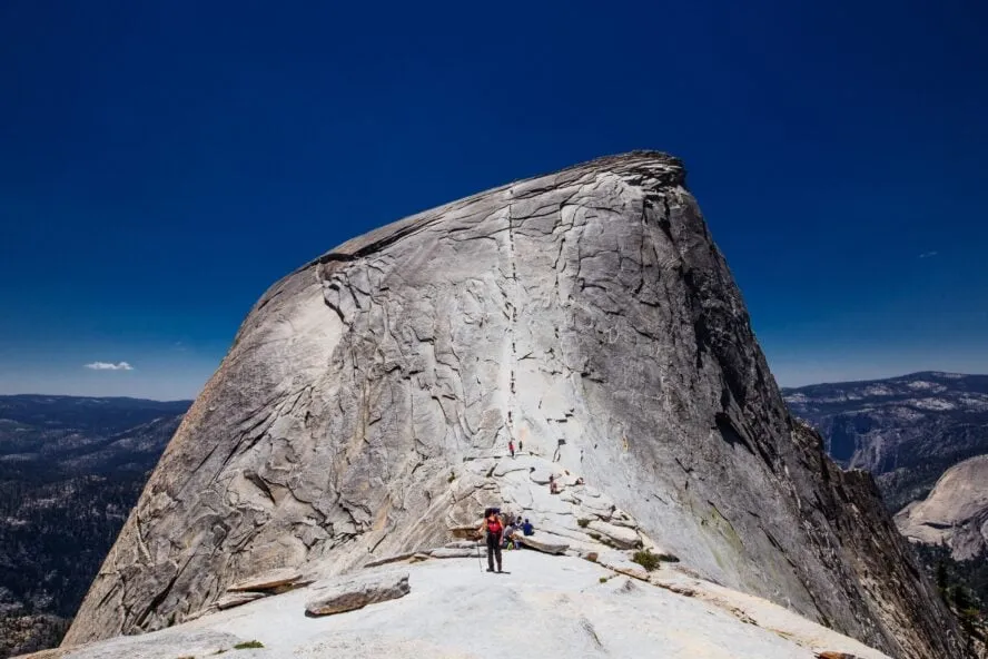 Hikers climbing the cables section of Half Dome in Yosemite National Park with dramatic granite cliffs
