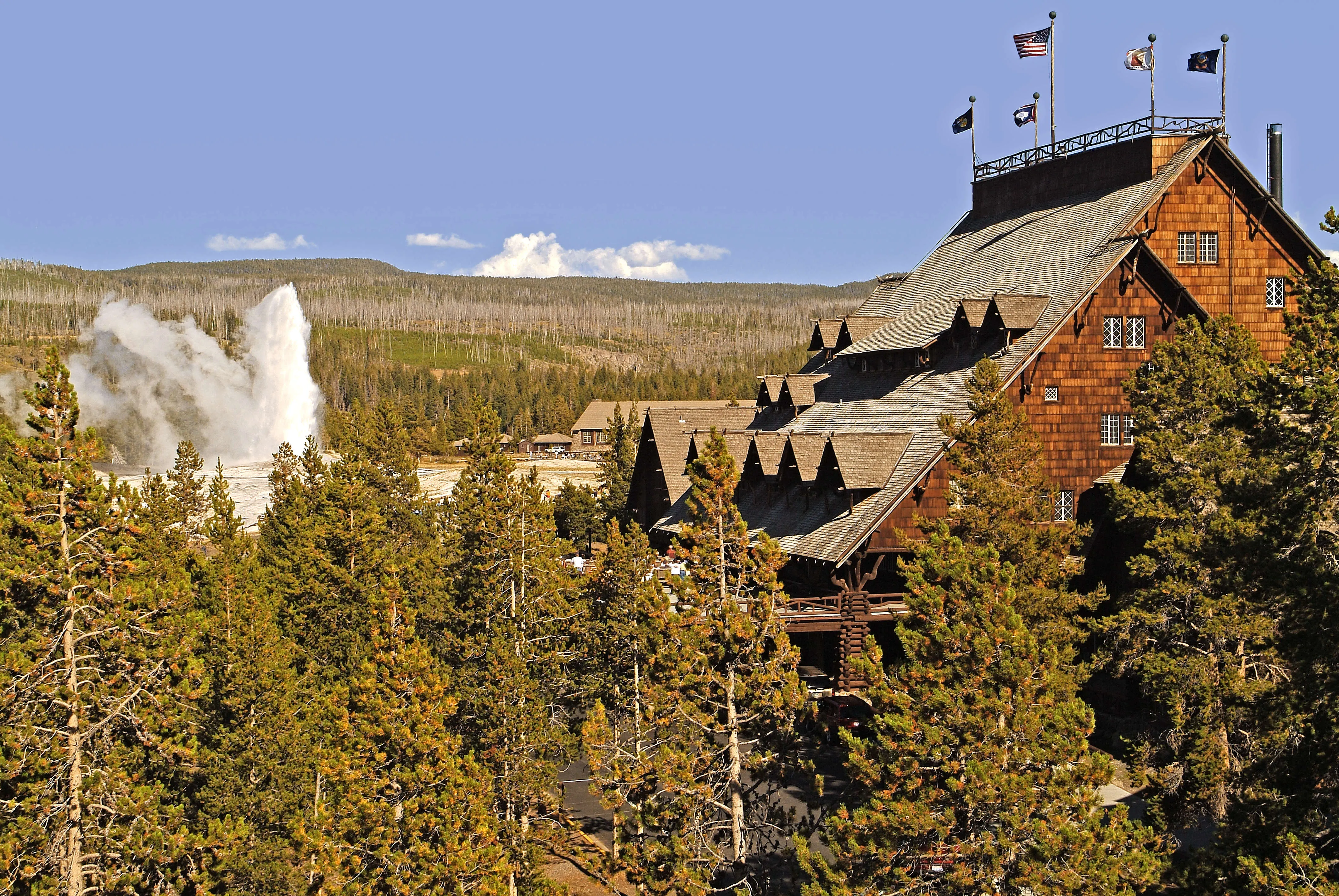 Old Faithful Inn exterior with Old Faithful Geyser and surrounding trees in Yellowstone National Park